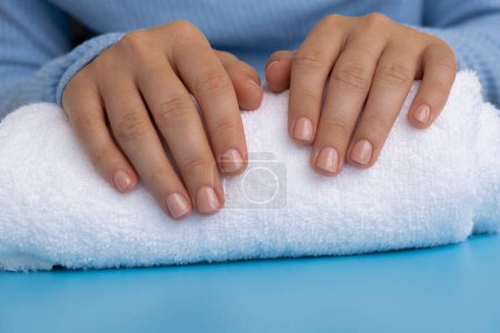 Woman manicured hands, stylish beige nails. Closeup of manicured nails of female hand in blue sweater in blue background. Winter or autumn style of nail design concept. Beauty treatment.