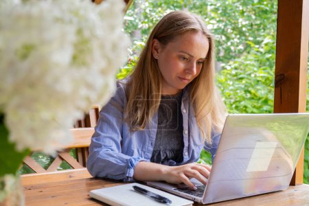 Junge, glückliche Frau konzentriert sich auf ihren Laptop in einer hölzernen Nische. Entspanntes Outdoor-Ambiente betont Komfort und Produktivität. Konzept zur Fernbedienung