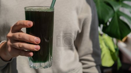 Eine unkenntliche Frau trinkt ein natürliches Bio-Pulver aus grünen Spirulina-Algen auf neutralem beigem Hintergrund. Chlorella Algen vegane Superfood Cocktails Smoothie Ergänzung Quelle und Entgiftungsgetränk