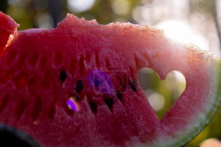 Sommer saisonales Essen. Saftige rote Wassermelonenscheibe in Herzform geschnitten im Freien Sommerurlaub Sonnenstrahlen. Konzept, den Moment an frischer Luft zu genießen. Nachhaltig ruhiger Lebensstil