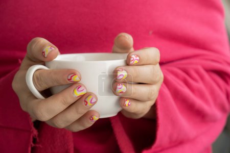 Foto de Elegantes uñas femeninas de verano de colores sosteniendo la taza blanca de café o té. Moderno de moda elegante Hermosa manicura. Lindo concepto de diseño minimalista de uñas pastel de tratamiento de belleza. Clavos de gel. Piel - Imagen libre de derechos