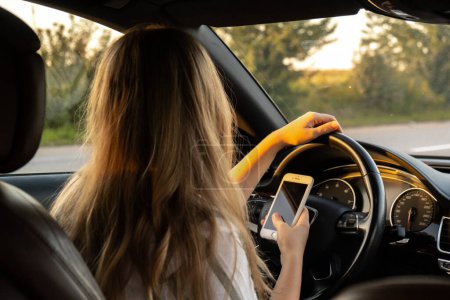 Mujer que envía mensajes con el teléfono inteligente mientras conduce el automóvil. Conductora usando teléfono móvil en la carretera durante la conducción del coche. Concepto de seguridad y tecnología 