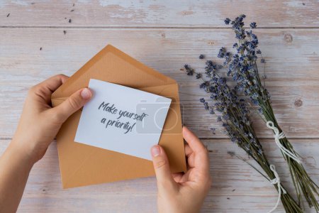 MAKE YOURSELF A PRIORITY text on supportive message paper note reminder from beige envelope. Flat lay composition dry lavender flowers. Concept of inner happiness, slowing-down digital detox personal