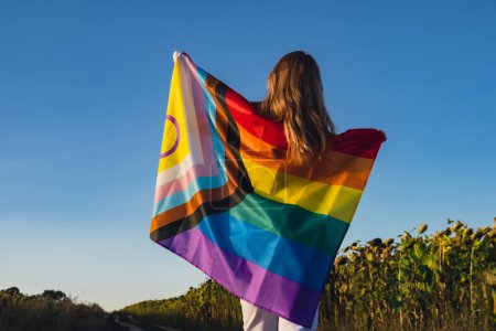 Mädchen zeigt ihre Geschlechtsidentität. Junge Frau steht mit Stolz Flagge Rainbow LGBTQIA Flagge aus Seidenmaterial auf Feld Hintergrund. Symbolmonat des LGBTQ-Stolzes. Gleiche Rechte. Frieden und Freiheit