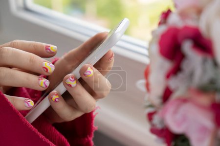Femme mains soignées tenant téléphone mobile, ongles colorés d'été élégants. Gros plan des ongles manucurés de la main féminine. Style d'été du concept de conception des ongles. Traitement beauté.