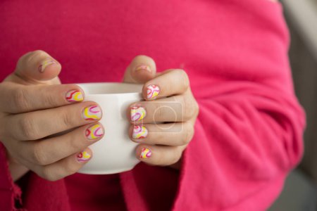 Pastel softness colorful manicured nails. Woman holding white cup of coffee or tea showing her new summer manicure in colors of pastel palette. Simplicity decor fresh spring vibes earth-colored