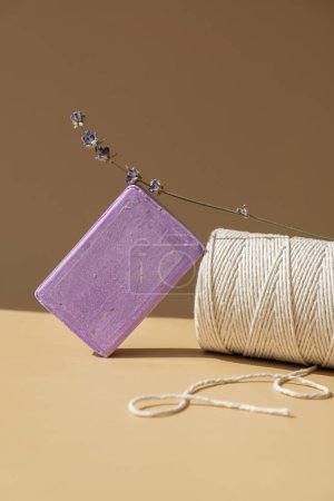 Lavender soap on beige background with spool of white cotton rope copy space for your text. Advertisement template mock up. Skincare homemade natural cosmetic concept. Organic dry lavender flower