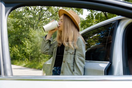 Smiling young woman drinking coffee or tea from reusable thermos cup. Traveler making a coffee break in Local solo travel on weekends concept. Exited woman explore freedom outdoors in forest. Unity
