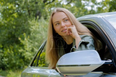 Blonde Frau ragt Kopf aus Windschutzscheibe Auto. Junge Touristen erkunden die lokale Reisewelt und erleben echte Augenblicke. Wahre Emotionen, die sich an der frischen Luft entspannen und erfrischen