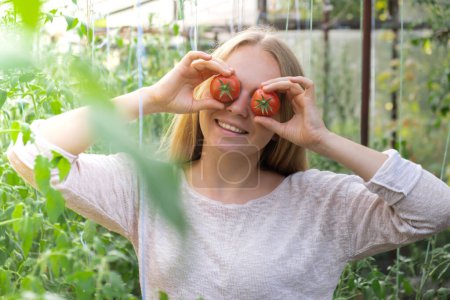 Lächelnder Landwirt mit Tomaten über den Augen im Gewächshaus. Ernte frisches Gemüse der Saison. Nahrungsmittel und Anbau. Nachhaltige Landwirtschaft