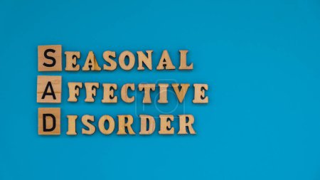 Seasonal affective disorder - text of wooden blocks on blue bright background. Concept of depression mood stress and anxiety. SAD wellbeing 