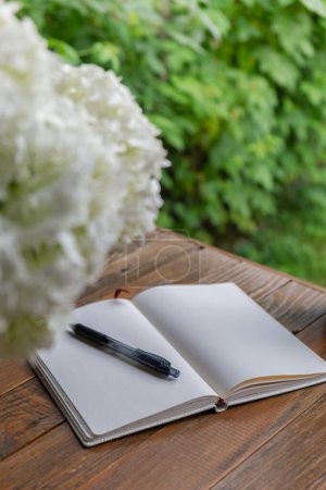 Open white empty paper notepad on wooden table outdoors. Concept of author writing in relaxed cozy atmosphere. Spiritual health digital detox slowing down practices 