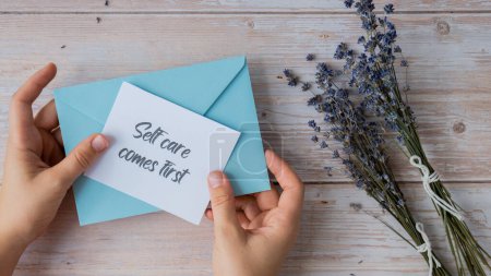 SELF CARE COMES FIRST text on supportive message paper note reminder from blue envelope. Flat lay composition dry lavender flowers. Concept of inner happiness, slowing-down digital detox personal