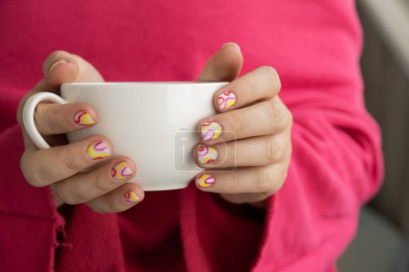 Stylish colorful summer female nails holding white cup of coffee or tea. Modern trendy stylish Beautiful manicure. Cute pastel nail minimalistic design concept of beauty treatment. Gel nails. Skin