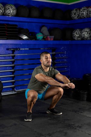 Photo for Vertical image of a latin man doing squats, wearing sportswear in a crossfit gym - Royalty Free Image