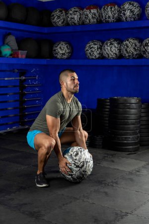 Photo for Latin man exercising in a gym, using a crossfit medicine ball - Royalty Free Image