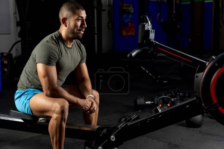 Photo for Sporty man, watching the board of a rower in the gym - Royalty Free Image