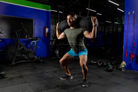 Photo for Man in sportswear in a gym doing squats with a sandbag on his back - Royalty Free Image