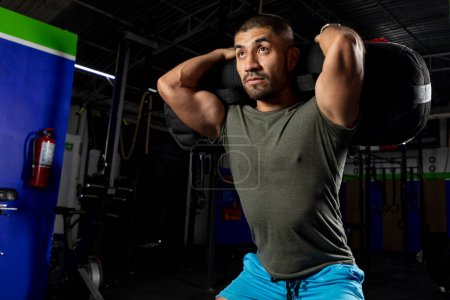 Photo for Close up of a man in sportswear in a gym doing squats with a sandbag on his back - Royalty Free Image