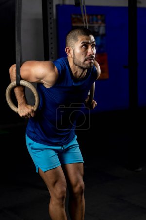 Photo for Vertical shot of a gymnast doing ring dips in the haros of a gym - Royalty Free Image