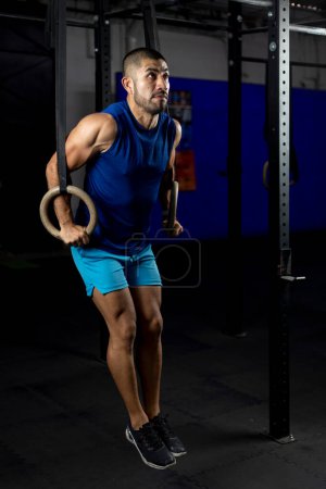 Photo for Vertical shot of a gymnast doing ring dips in the haros of a gym - Royalty Free Image