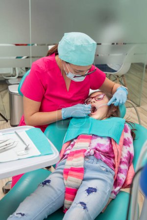Photo for Vertical image of a dentist checking a girls mouth in her office. - Royalty Free Image