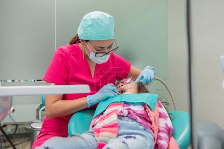 Photo for Dentist giving oral treatment to a young girl in his dental office - Royalty Free Image