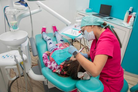 Photo for Latina dentist cleaning a girls teeth with a contra angle, in her office - Royalty Free Image