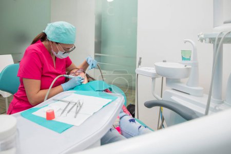 Photo for Latina woman dentist, cleaning a girls teeth in her medical office, with copy space. - Royalty Free Image