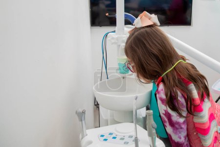 Photo for Girl rinsing her mouth in the sink at the dentists office - Royalty Free Image