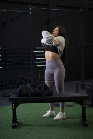 Mujer atleta quitándose la sudadera en el gimnasio, para entrenar.