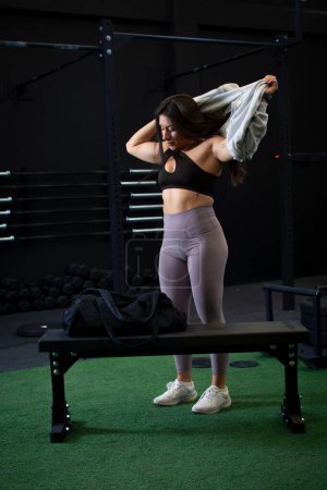 Foto de Una mujer con un cuerpo atlético cambia su ropa deportiva para comenzar su entrenamiento en el gimnasio. - Imagen libre de derechos