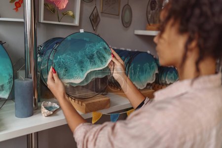 Foto de Female decorator puts handmade epoxy resin tray on stand exposition in studio. High quality photo - Imagen libre de derechos