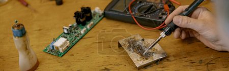 Photo for Close up of repairman hands is soldering circuit board of electronic device on the table in workshop - Royalty Free Image