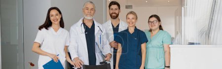 Photo for Group of professional doctors in uniform standing in clinic hall with medical wheelchair in clinic - Royalty Free Image