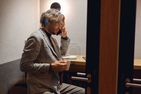 Foto de Empresario hablando de teléfono con el cliente mientras está sentado en coworking y trabajando en el ordenador portátil - Imagen libre de derechos