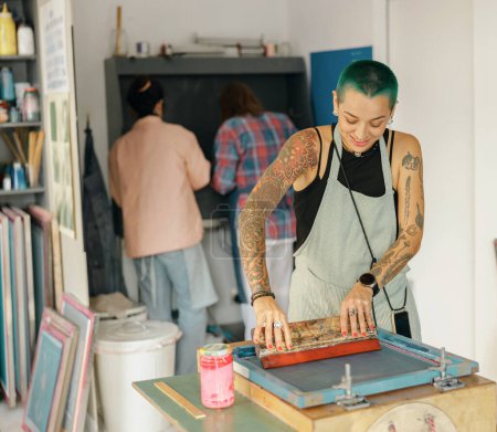 Eine Arbeiterin mit Rakel drückt Tinte auf einen Rahmen, der im Designstudio arbeitet. Siebdruck