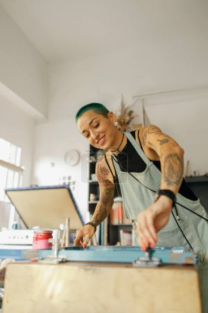 Arbeiterin mit Rakel druckt in einem Designstudio Bilder auf Textilien im Siebdruckverfahren