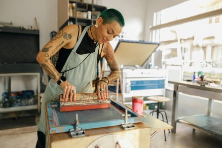 Eine Arbeiterin mit Rakel drückt Tinte auf einen Rahmen, der im Designstudio arbeitet. Siebdruck