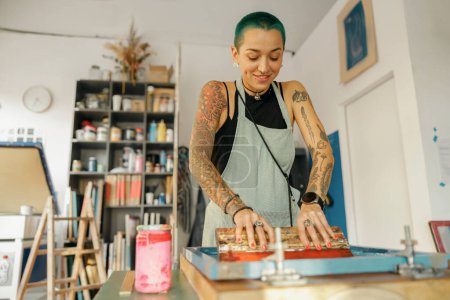 Arbeiterin mit Rakel druckt in einem Designstudio Bilder auf Textilien im Siebdruckverfahren
