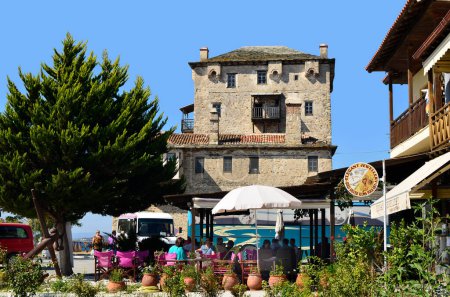 Photo for Ouranoupoli, Greece - September 29, 2011: unidentified tourists in a restaurant in front of the Prosphorios-Tower, the landmark of the village on the border to Holy Mount Athos - Royalty Free Image