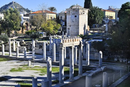 Athens, Greece - December 19, 2023: Ruins in the ancient Roman Agora in Plaka district with Tower of the Winds, entrance to old Madrasa Gate and Lycabettus Hill in background