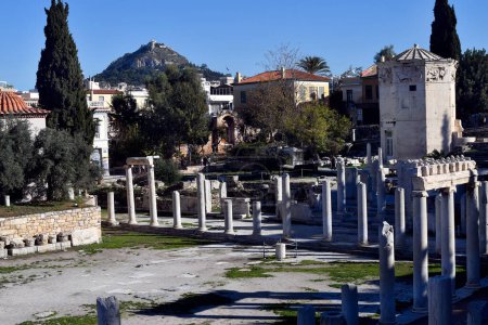Athens, Greece - December19, 2023: Ruins in the ancient Roman Agora in Plaka district with Tower of the Winds, entrance to old Madrasa Gate and Lycabettus Hill in background