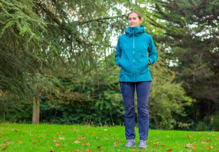 a young woman in a sports tourist jacket stands on a meadow near a forest. nature, hiking, active lifestyle, camping