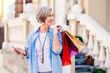 Beautiful and happy senior adult woman shopping in the city - Stylish fashionable old mature people shopping in clothing store
