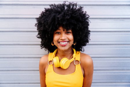 Schöne junge glückliche Afrikanerin mit Afro-Lockenfrisur schlendert durch die Stadt - Fröhliches schwarzes Studentenporträt auf buntem Wandhintergrund