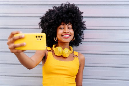 Schöne junge glückliche Afrikanerin mit Afro-Lockenfrisur schlendert durch die Stadt - Fröhliches schwarzes Studentenporträt auf buntem Wandhintergrund