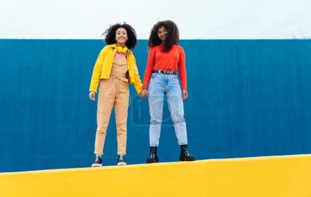 Photo for Young happy women posing on colored blue and yellow colored walls. Teenagers girl spending time together after school - Royalty Free Image