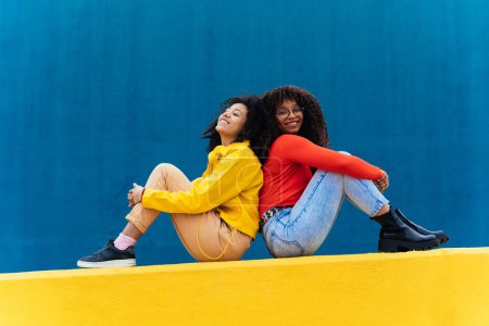 Téléchargez les photos : Jeunes femmes heureuses posant sur des murs colorés bleus et jaunes. Les adolescentes passent du temps ensemble après l'école - en image libre de droit