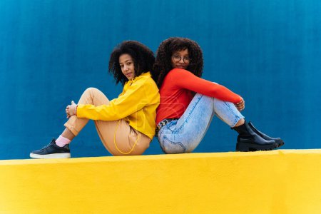 Foto de Mujeres jóvenes felices posando en paredes de color azul y amarillo. Adolescentes chica pasar tiempo juntos después de la escuela - Imagen libre de derechos